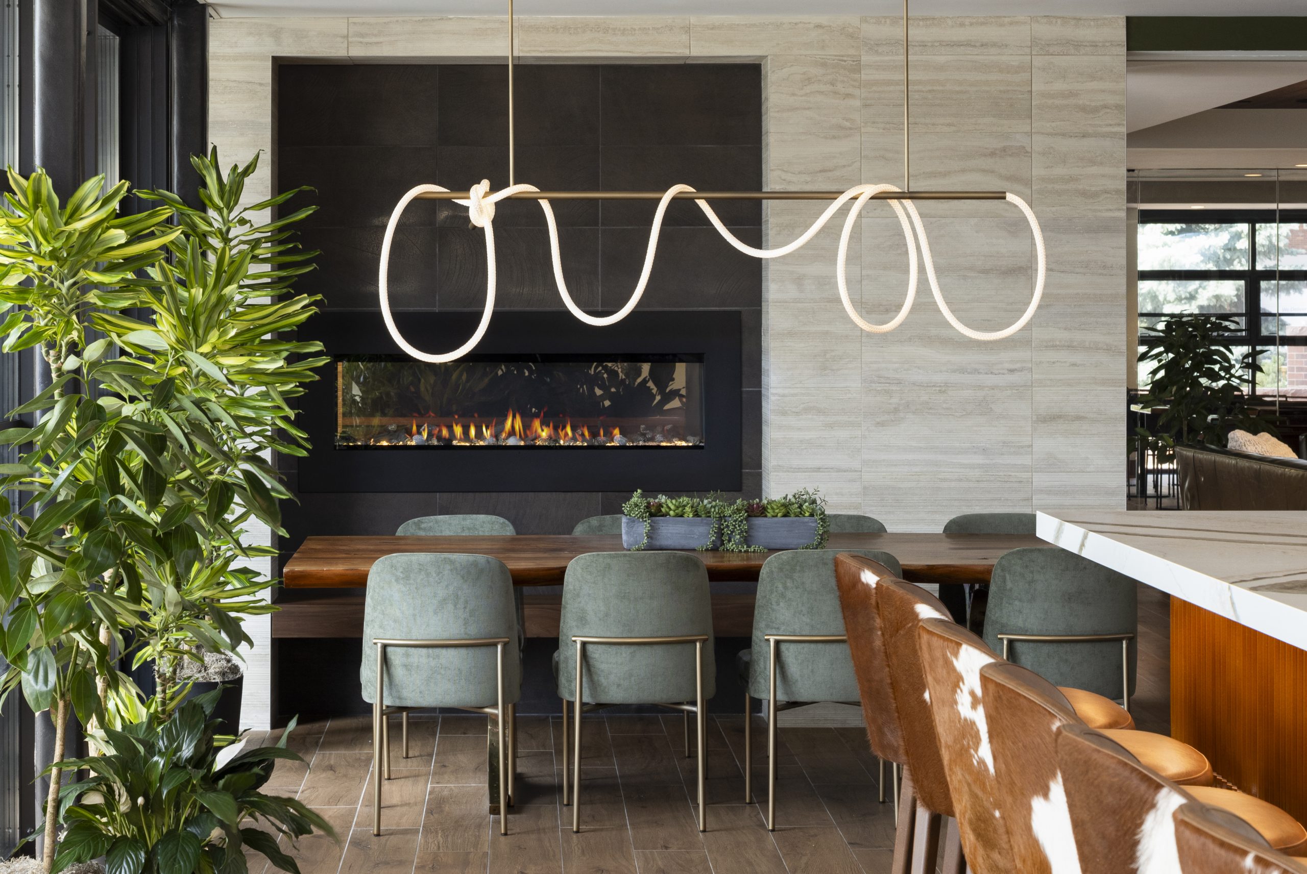 Modern dining bar interior with wood table, green chairs, sculptural LED chandelier, and fireplace. Nature inspired design by Mountain Lily Studios.